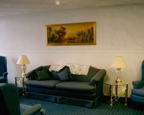 Blue upholstered sofa and armchairs with side tables, lamps, and a landscape painting on the wall in a lounge.
