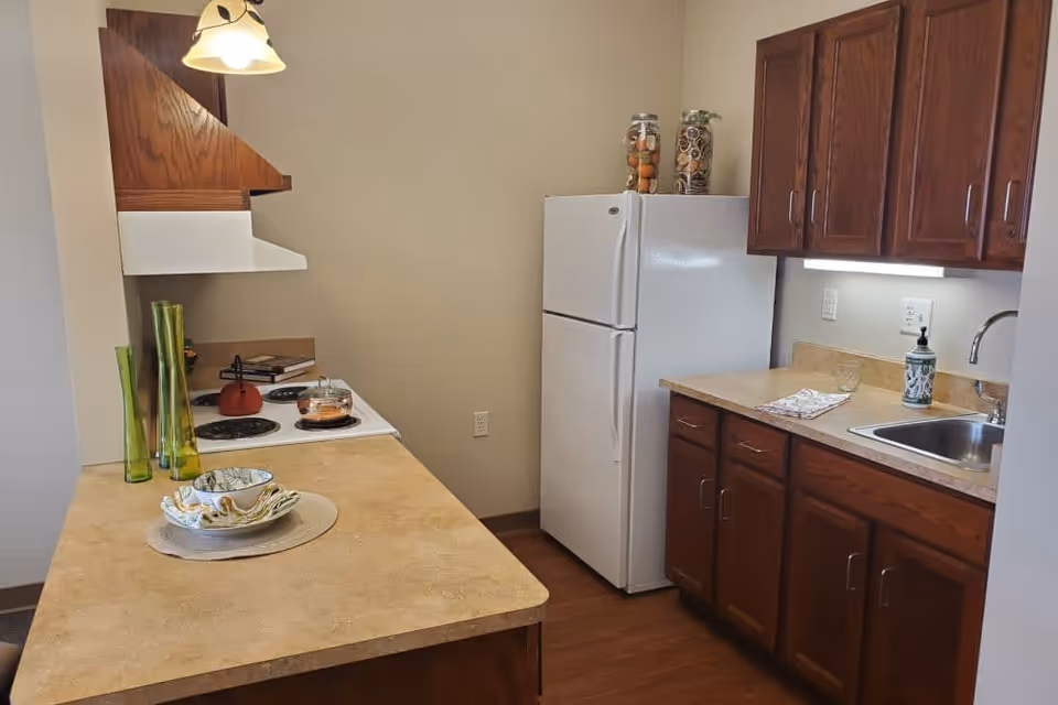 Compact kitchen with a white refrigerator and stove, wooden cabinets, sink, and a countertop set with dishes and decorative vases.