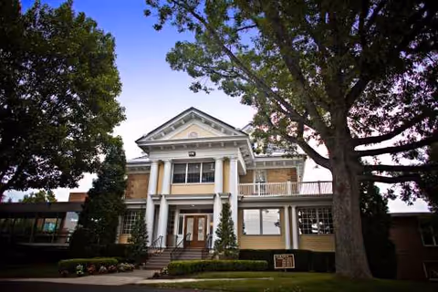 Front view of a two-story building with columns and surrounding trees.