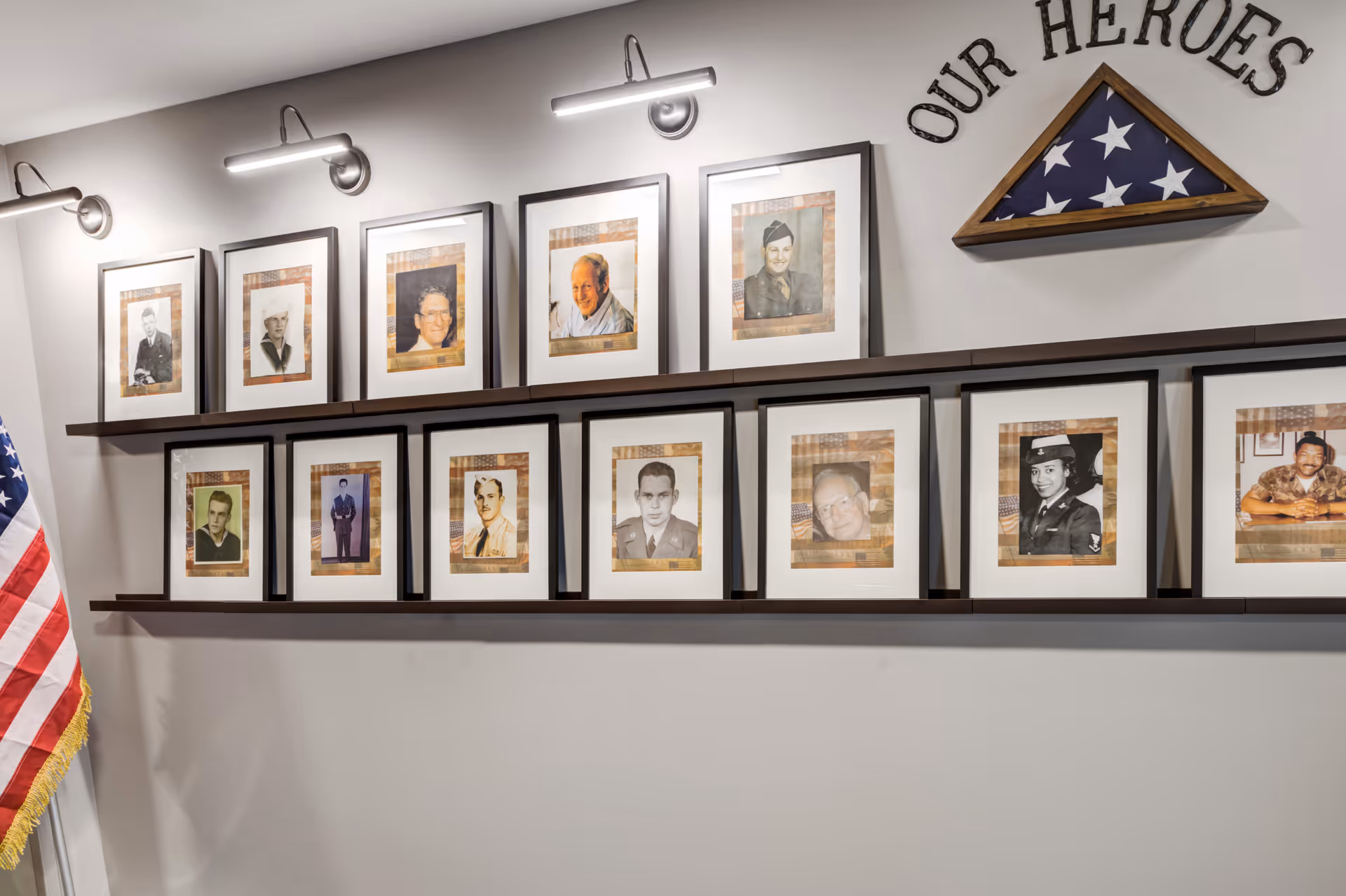 Wall display with framed portraits of veterans, a folded American flag in a triangular case, and an 'OUR HEROES' sign.