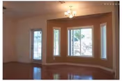 Empty living room with a bay window and glass door, hardwood floors, and a ceiling light fixture.