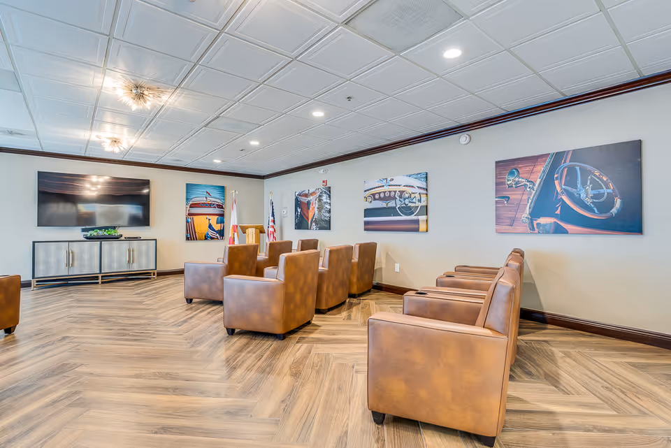 Community lounge with brown leather armchairs arranged facing a wall-mounted TV and artwork on the walls.