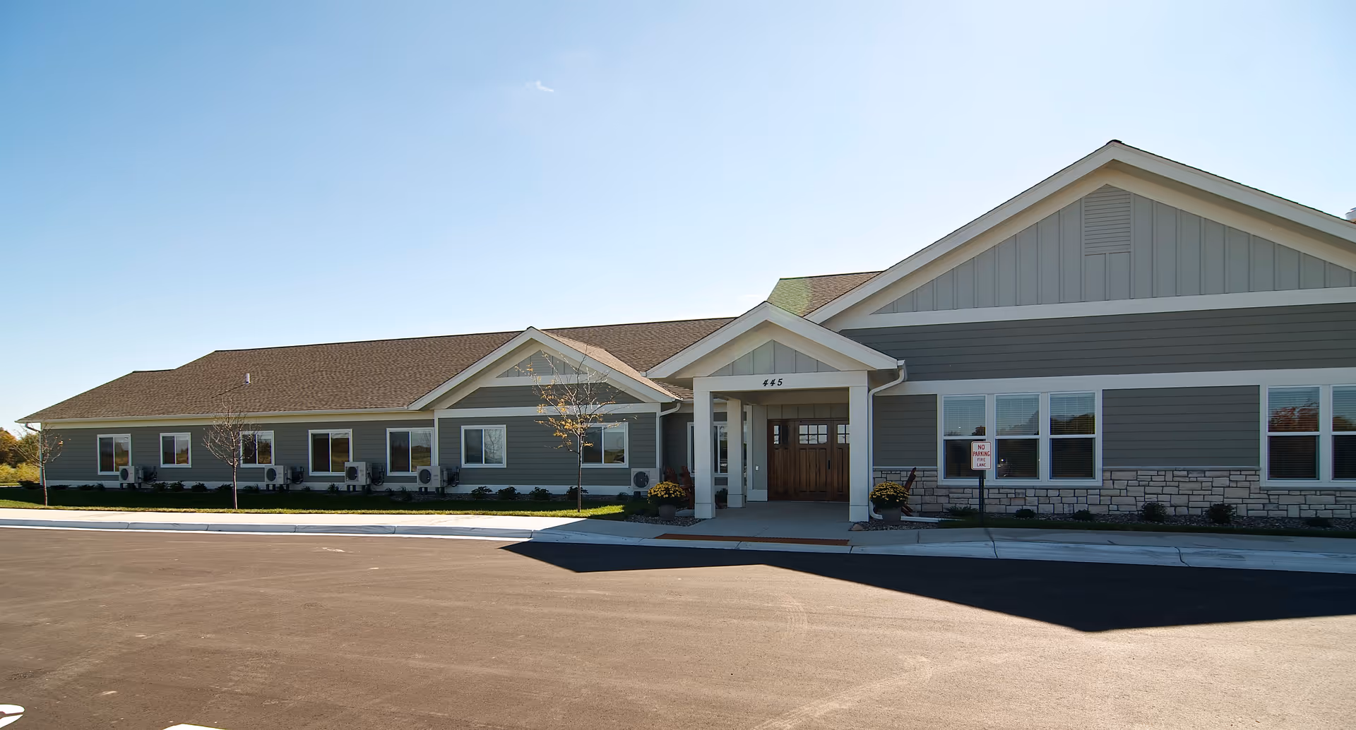 Single-story senior living facility building with a covered entrance, multiple windows, and a paved driveway under a clear sky.