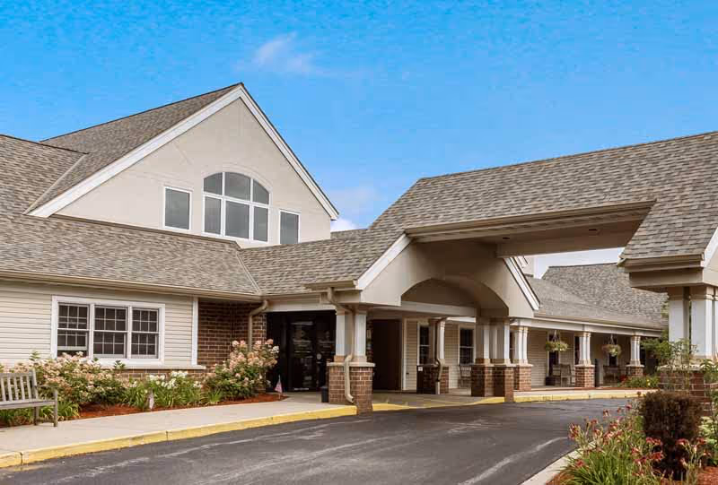 Front entrance of a single-story healthcare building with a covered drive-up porte-cochere, columns, and landscaped flower beds.