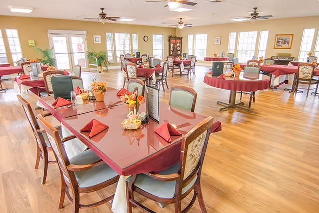 Bright dining room with multiple tables set with red napkins and autumn centerpieces.