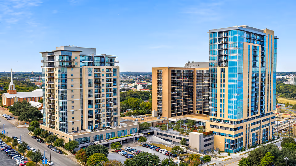 Exterior view of Trinity Terrace senior living campus with tall glass towers and connected buildings, parking lots, and landscaping.