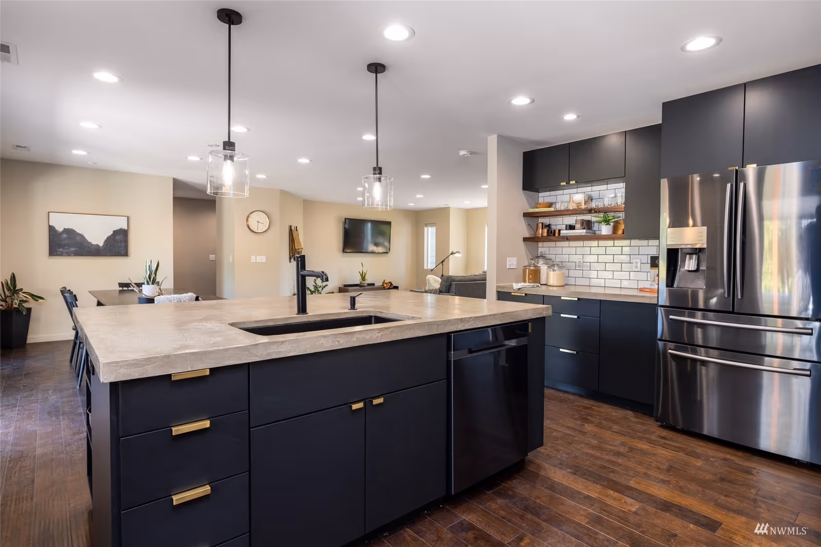 Modern open-concept kitchen with a large island, pendant lights, dark cabinetry and stainless steel appliances.