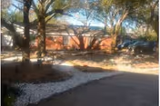 Single-story brick nursing facility building viewed from a driveway with trees and white gravel landscaping.