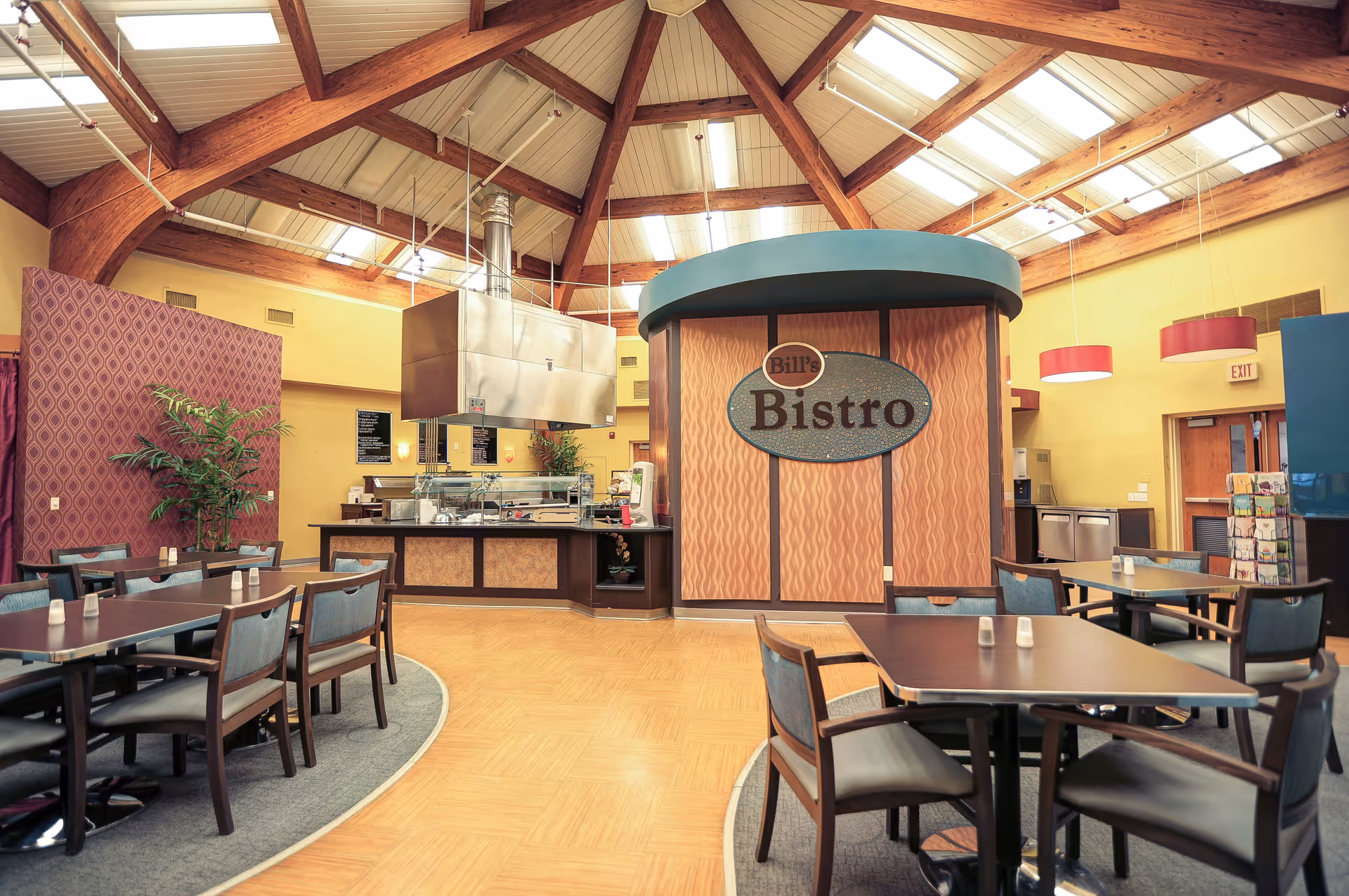 Dining area with tables and chairs and a central "Bill's Bistro" serving counter beneath a vaulted wooden ceiling.