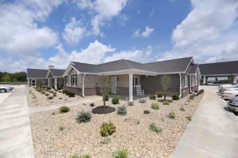 Front view of a villa-style senior living building with gravel landscaping and parked cars.