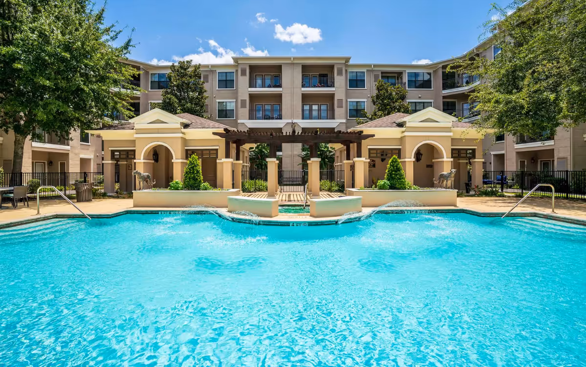 Outdoor swimming pool with a pergola and seating area in front of a multi-story senior living building.