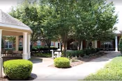 Courtyard with a covered gazebo, paved walkways, and manicured shrubs and trees in front of a brick residential building.
