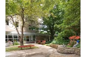 Outdoor courtyard area with trees, benches, and a stone planter wall in front of a building with large windows.