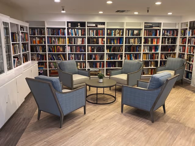 A cozy reading area with six armchairs arranged around a round coffee table in front of wall-to-wall bookshelves.