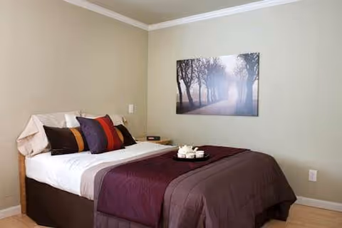 A neatly made bedroom with a framed nature scene above the bed and decorative pillows.