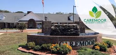 Exterior view of Caremoor Retirement Center with a brick fountain and flower beds.