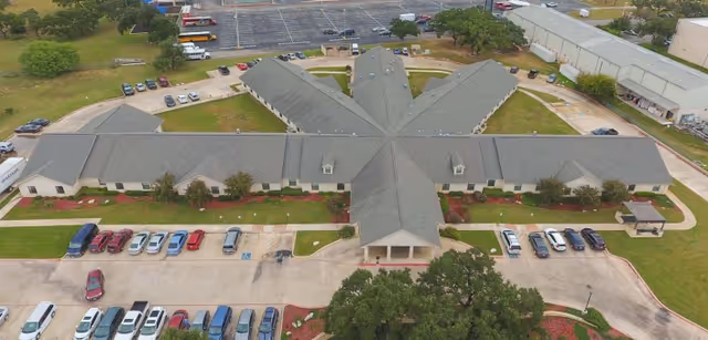 Aerial view of Sonterra Health Center, a single-story building with a star-shaped layout surrounded by parking lots and green lawns with trees and shrubs.