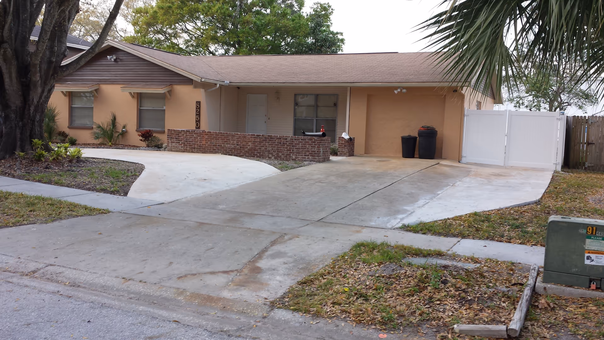 Single-story peach-colored building with a wide concrete driveway, brick planter and white side gate.