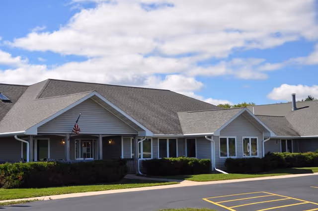 Single-story senior living facility exterior with a front entrance and trimmed hedges.