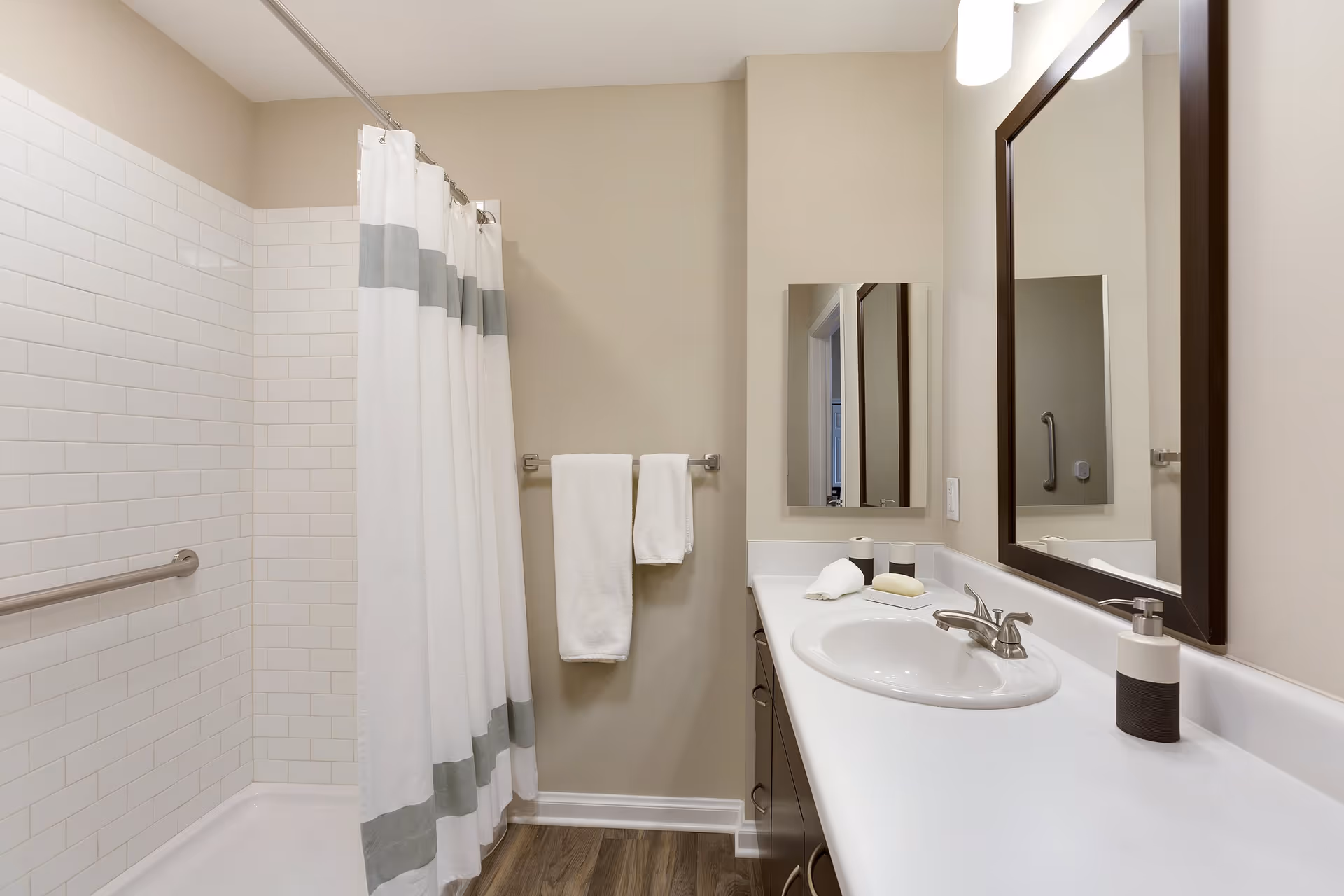 Bright modern bathroom with a shower and curtain, white sink and countertop, mirror, towel rack, and grab bar.