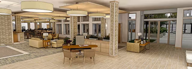 Spacious and well-lit interior common area of a senior living facility with multiple seating arrangements including tables with chairs, sofas, and armchairs. Large windows and glass doors provide natural light and views of an outdoor garden area. The space features modern lighting fixtures and neutral-toned decor.