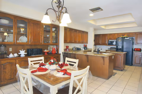 Dining area with wooden cabinets, a table set with red napkins and an island.