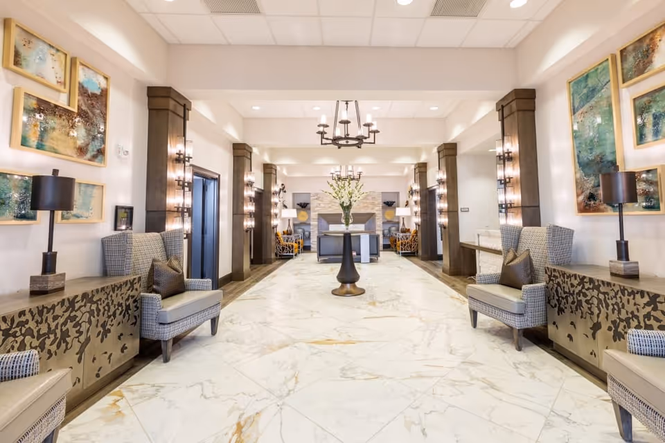 Bright, elegant lobby with marble floors, seating alcoves, chandeliers, and a central floral arrangement.