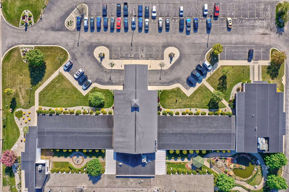 Aerial view of the Carriage House Nursing and Rehab building with parking lots, walkways, landscaped lawns and a small pond.