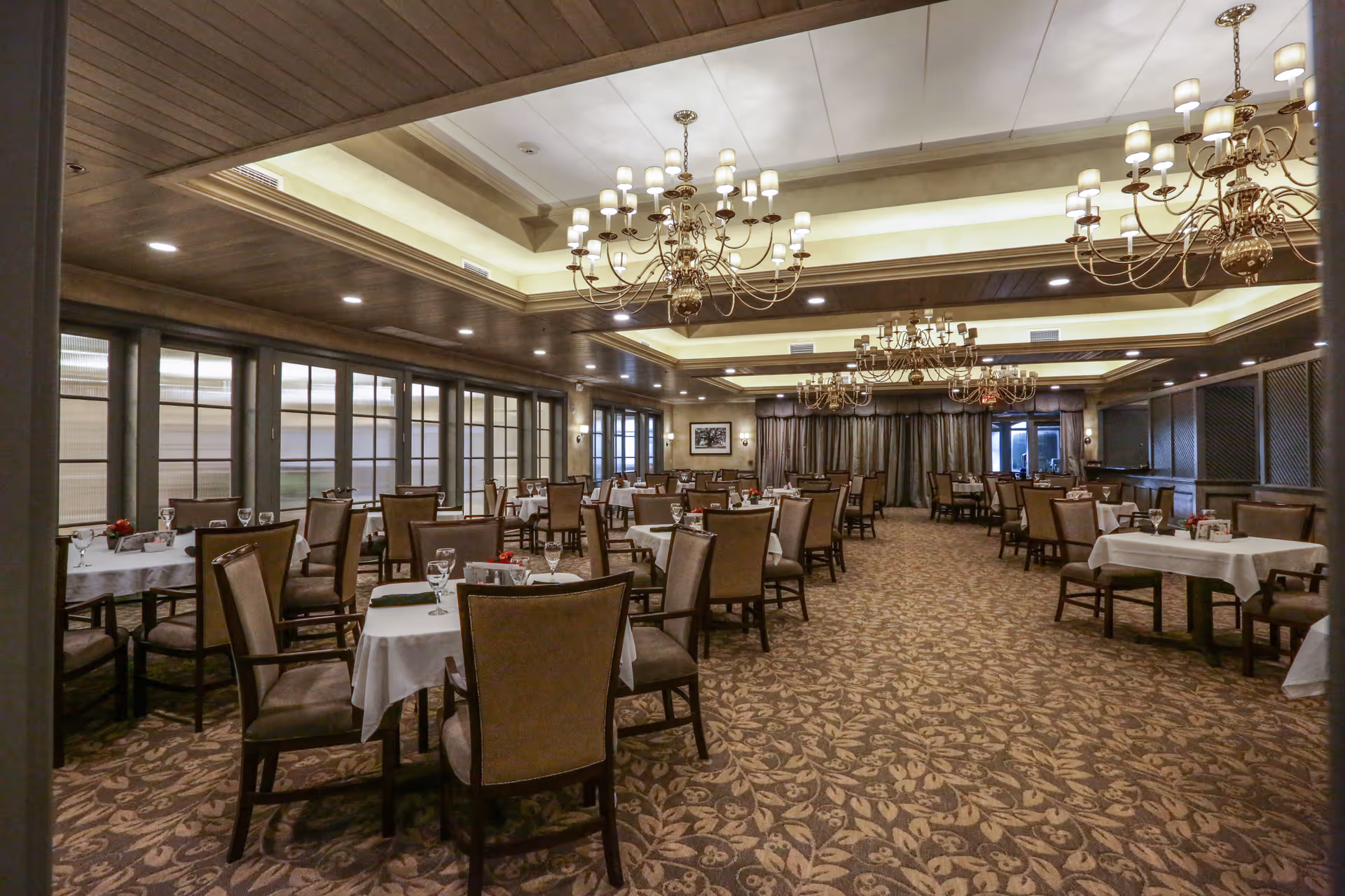 Spacious elegant dining room with multiple set tables, chandeliers, and patterned carpet.