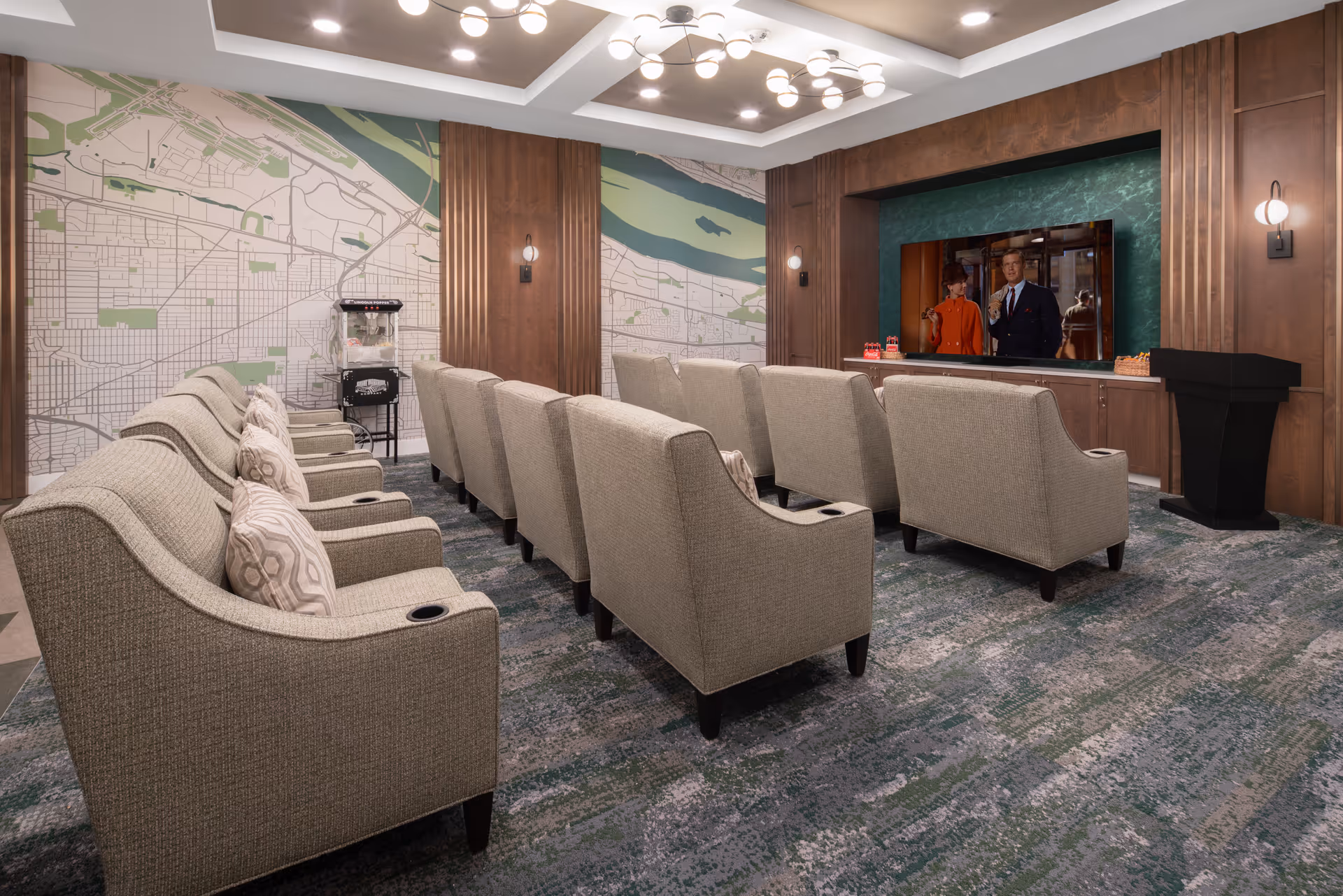 A cozy screening room with two rows of upholstered armchairs facing a large wall-mounted television and a popcorn machine by a muraled wall.