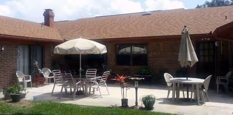 Brick building exterior with a concrete patio, tables, chairs, and umbrellas for outdoor seating.