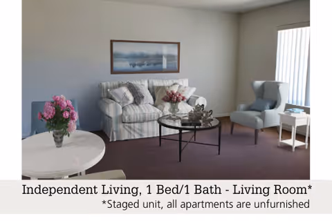 Staged living room with a striped sofa, armchair, round glass-top coffee table, side tables, and floral arrangements.