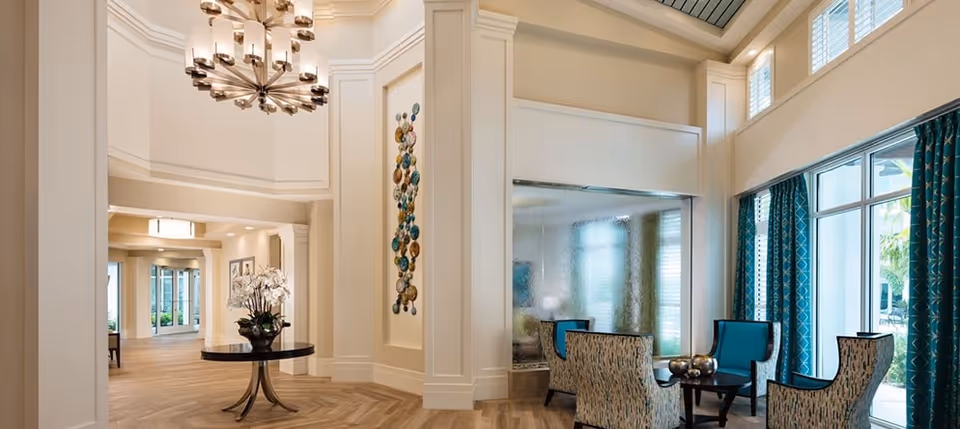 Elegant bright lobby with a chandelier, central round table, seating area, decorative wall art and large windows.