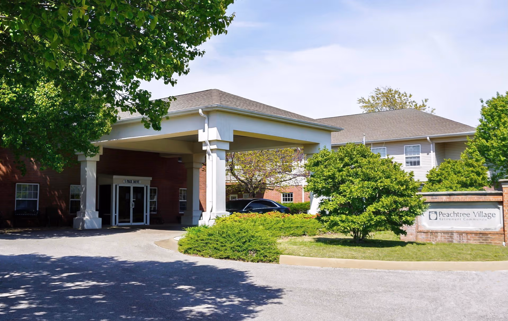 Front entrance of Peachtree Village assisted living showing a covered porte-cochere, landscaped driveway, and facility sign.