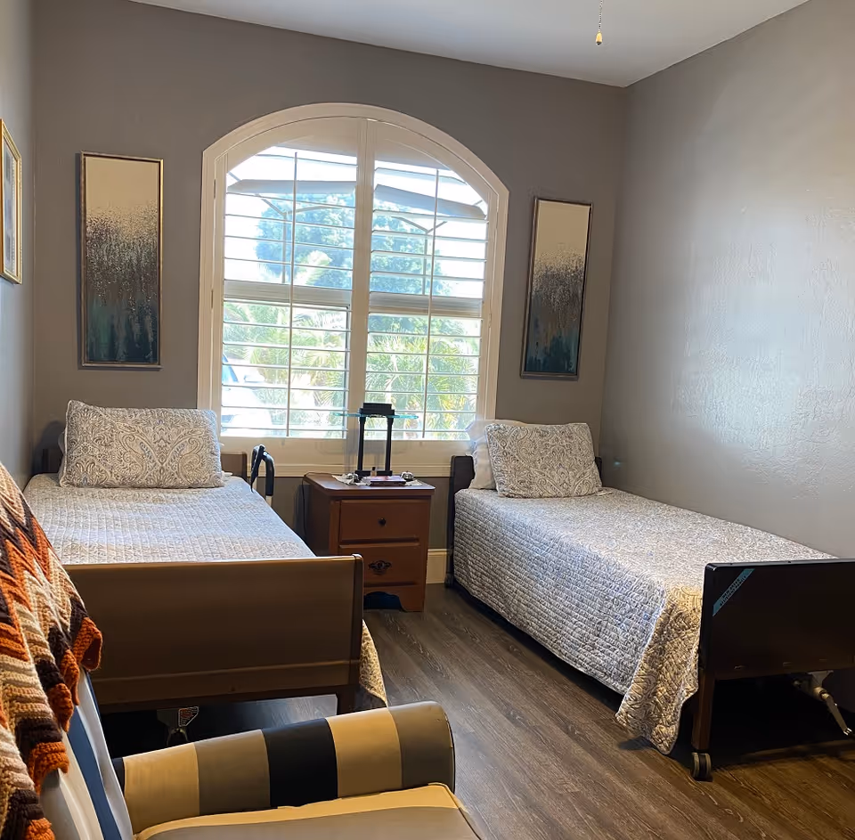Shared bedroom with two single beds, a nightstand, arched window, wall art, and wooden floor.
