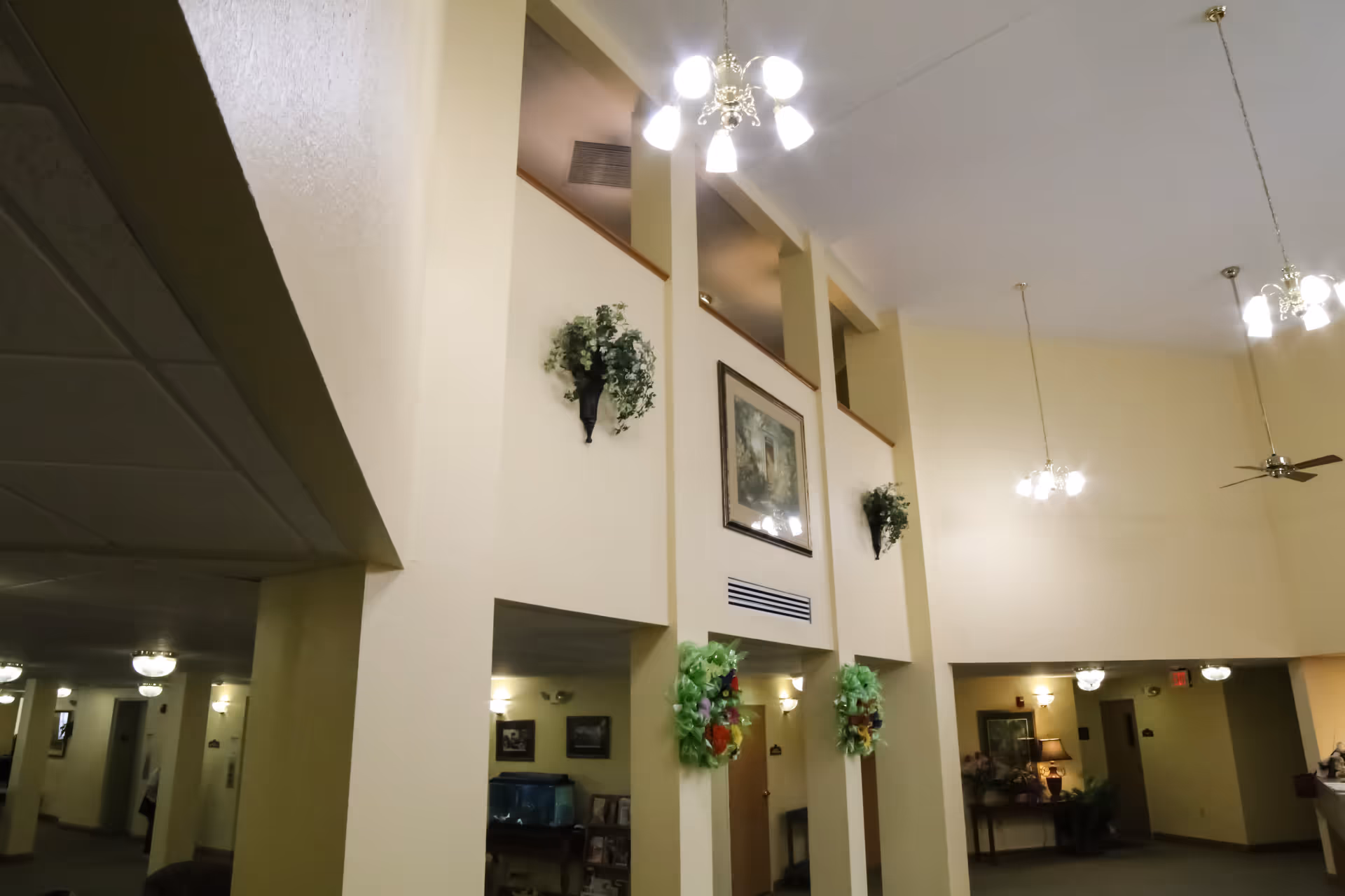 Spacious two-story interior common area with high ceilings, hanging chandeliers, columns, wall art and decorative plants.