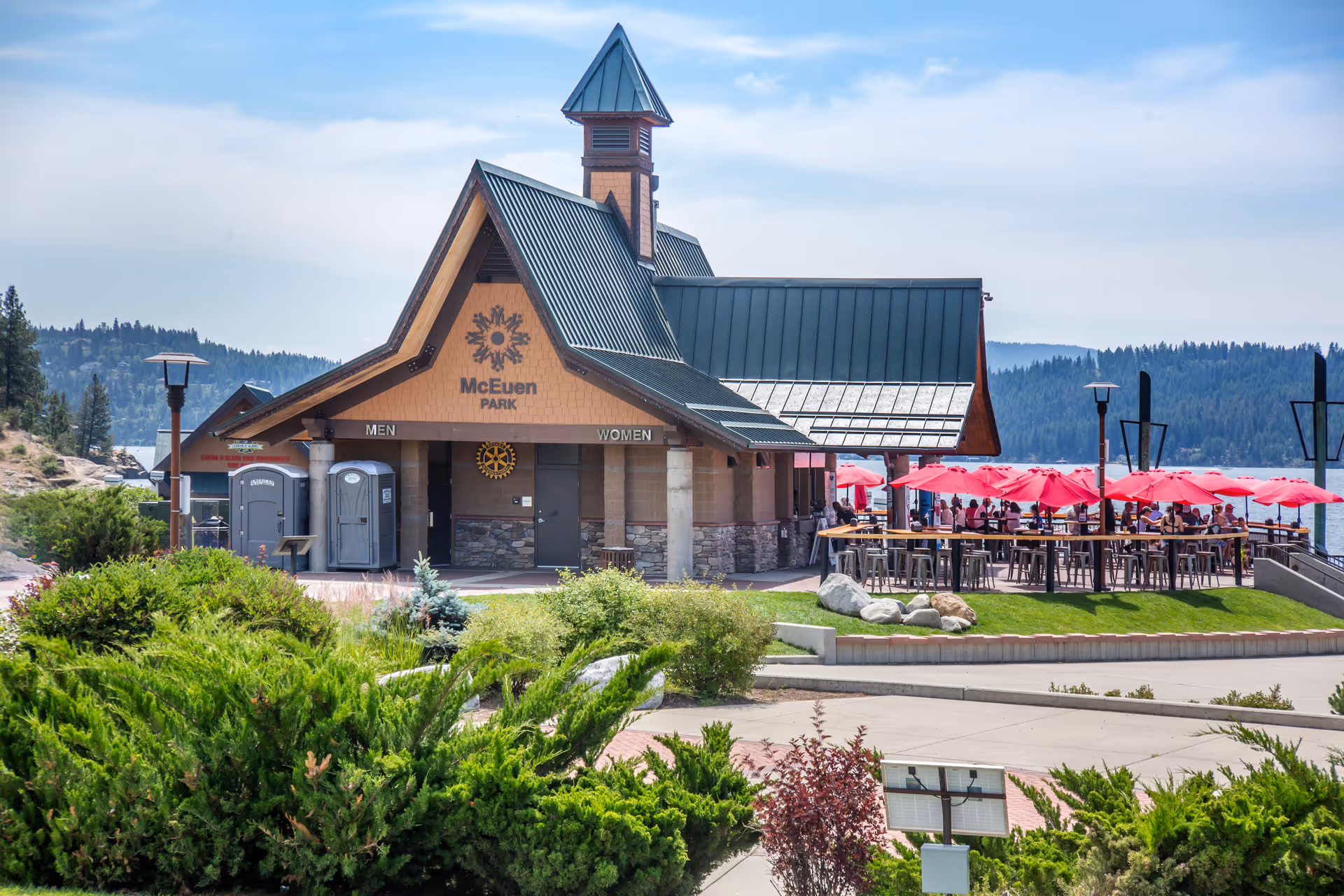 A lakeside park building labeled "McEuen Park" with outdoor dining under red umbrellas and landscaped foreground.
