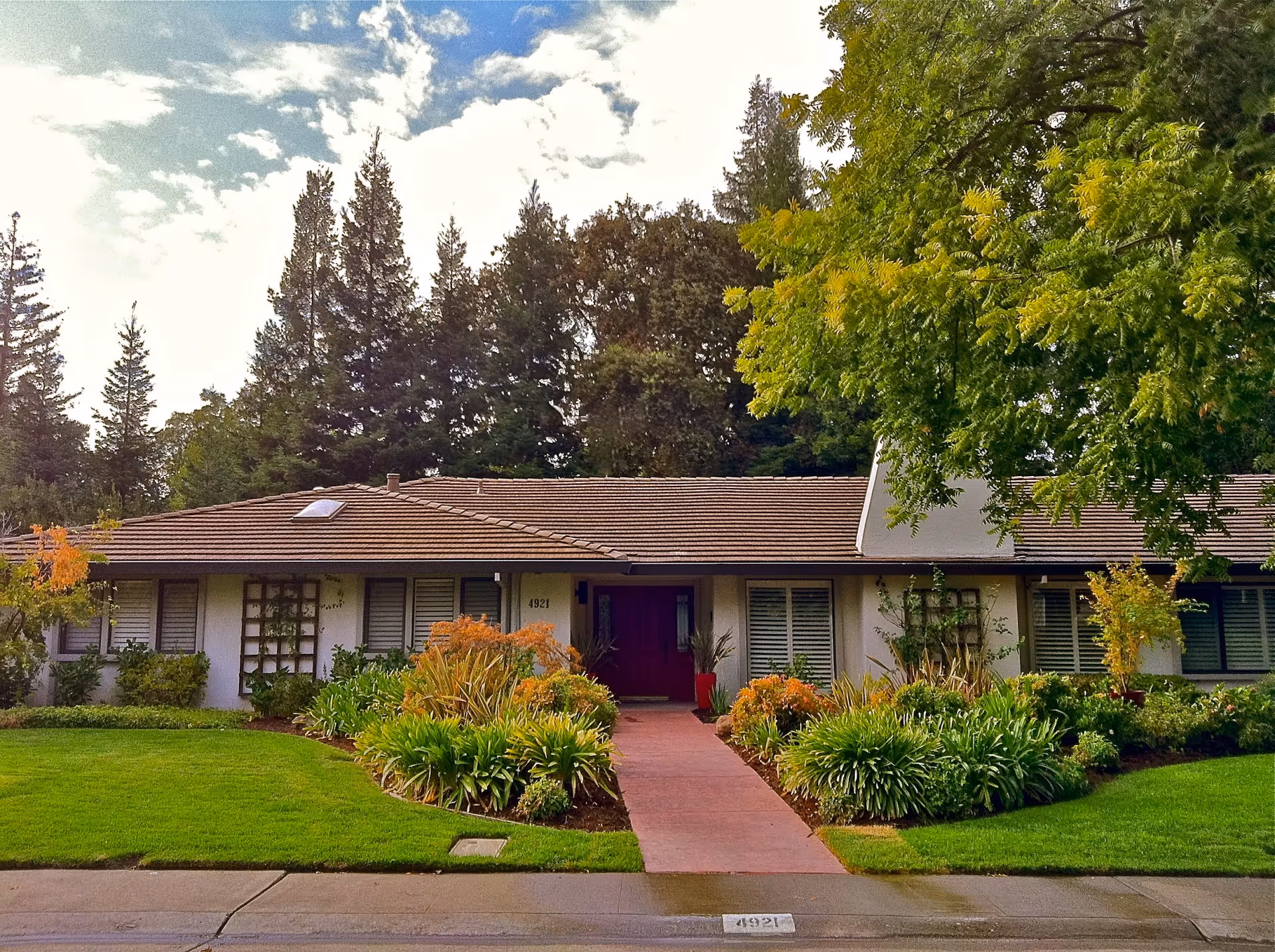 Single-story ranch-style building with a central red walkway, manicured lawn and landscaping, and trees in the background.