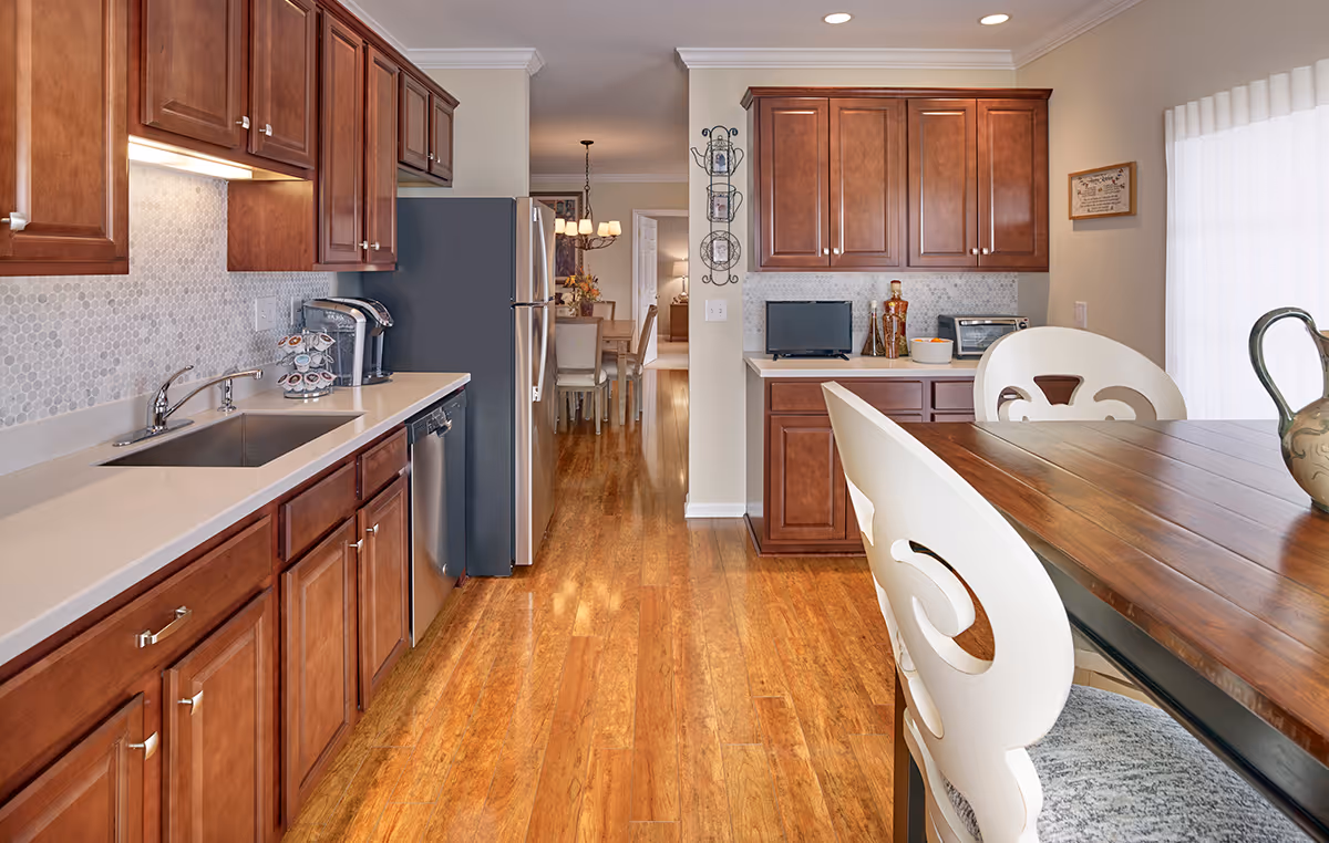 Well-lit modern kitchen with wooden cabinets, stainless steel appliances, and a dining table with white chairs.