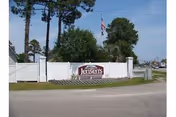 White fence entrance with a sign reading "Jensen's" and an American flag among trees behind it.