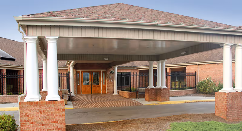 Covered entrance of a brick building with white columns and wooden double doors, part of Friendship Richfield Living - Joseph C Thomas Center.