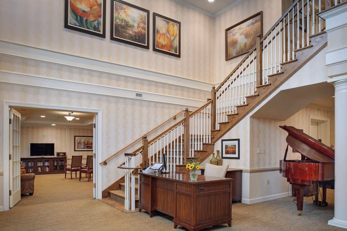 Sunny interior lobby featuring a wooden staircase, a reception desk with flowers, and a red grand piano.