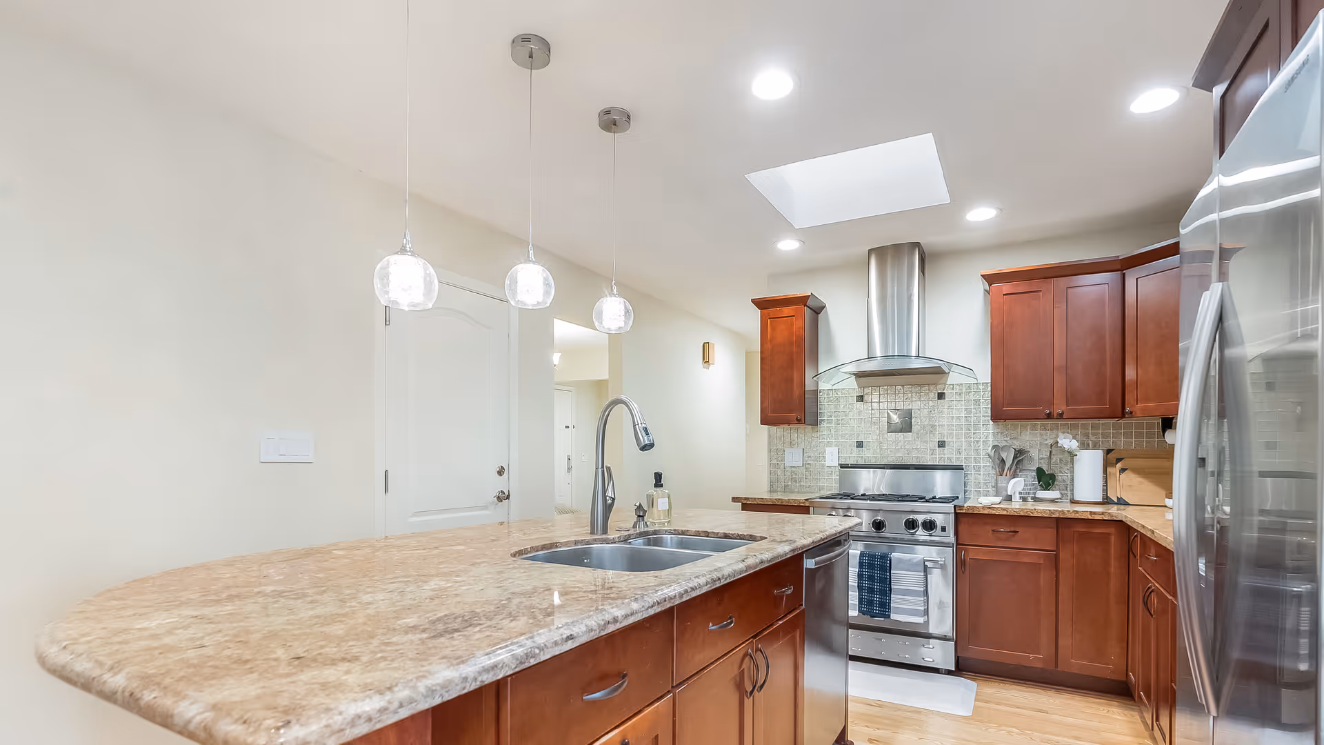Bright modern kitchen with a granite island, stainless steel appliances, and cherry wood cabinets.