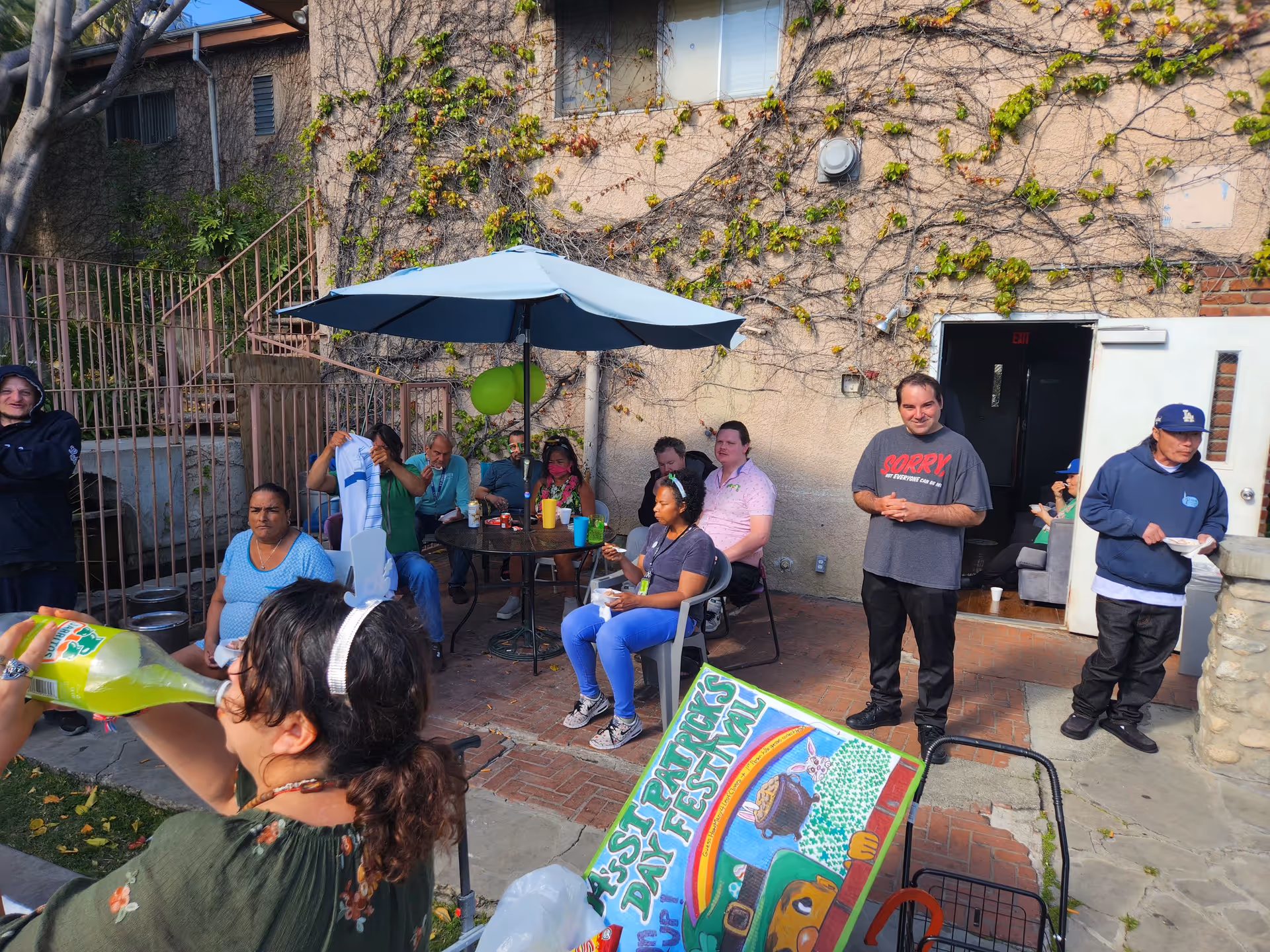A group of people gathered outside in a patio setting, some seated and others interacting, with decorations visible.