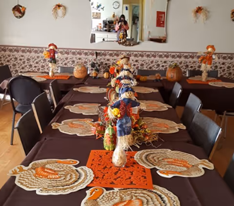 Long dining table set with turkey-shaped placemats and scarecrow centerpieces in a festive dining room with a wall mirror reflecting the photographer.