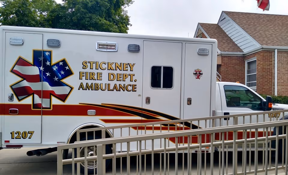 A Stickney Fire Dept. ambulance parked beside a brick building with a metal railing in the foreground.