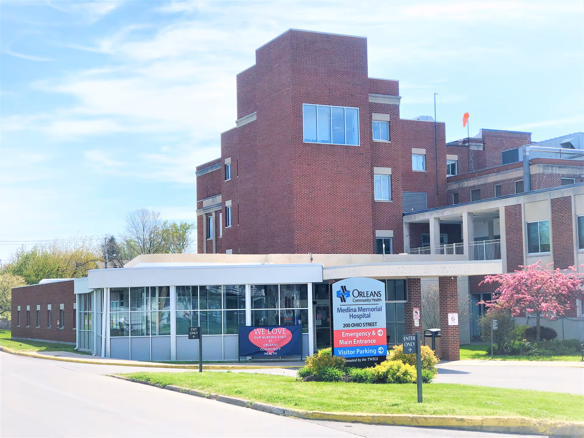 Front exterior of a red-brick hospital with a glass-walled entrance and a sign for Orleans Community Health Medina Memorial Hospital.