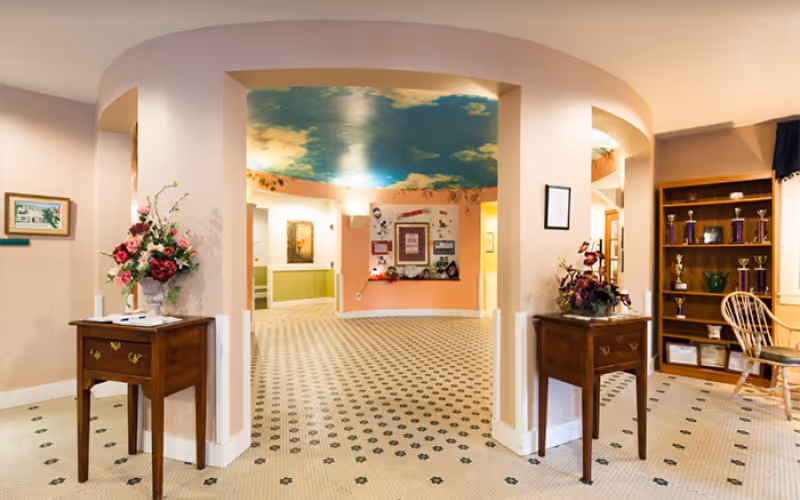 Interior view of the lobby at Gorham House, featuring a curved entrance, floral arrangements on wooden tables, and a ceiling painted with clouds.