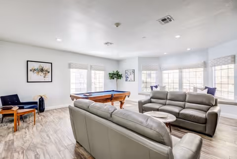 Bright communal lounge with leather sofas, a pool table, side chairs, and large windows letting in natural light.