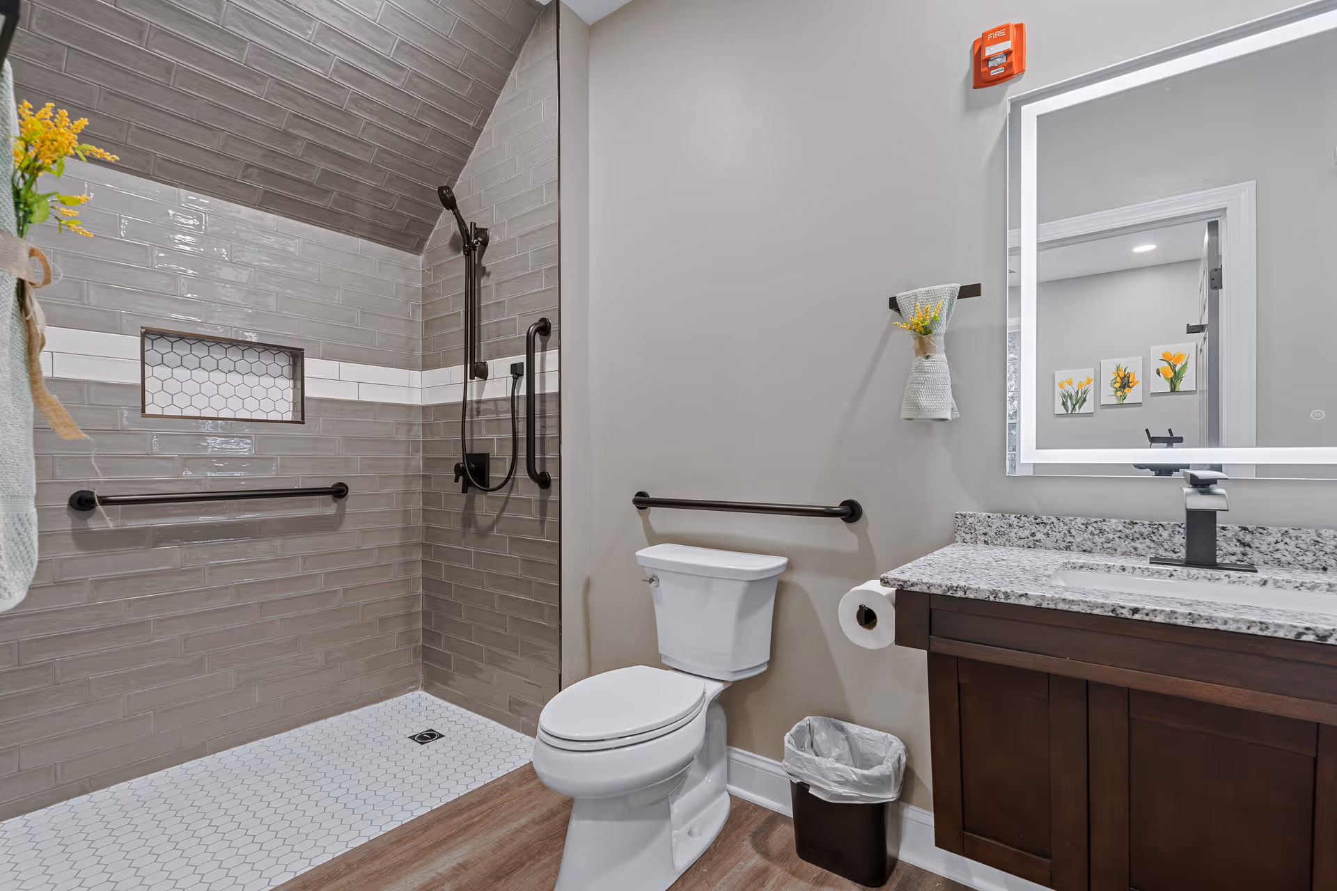 Accessible bathroom with a tiled walk-in shower, grab bars, toilet, and vanity with a lit mirror and granite countertop.
